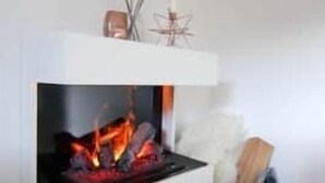 A modern fireplace with a white mantel, a small table with a decorative item, and a pair of candles on the floor. - Apartment Bergjuwel (Hermagor)