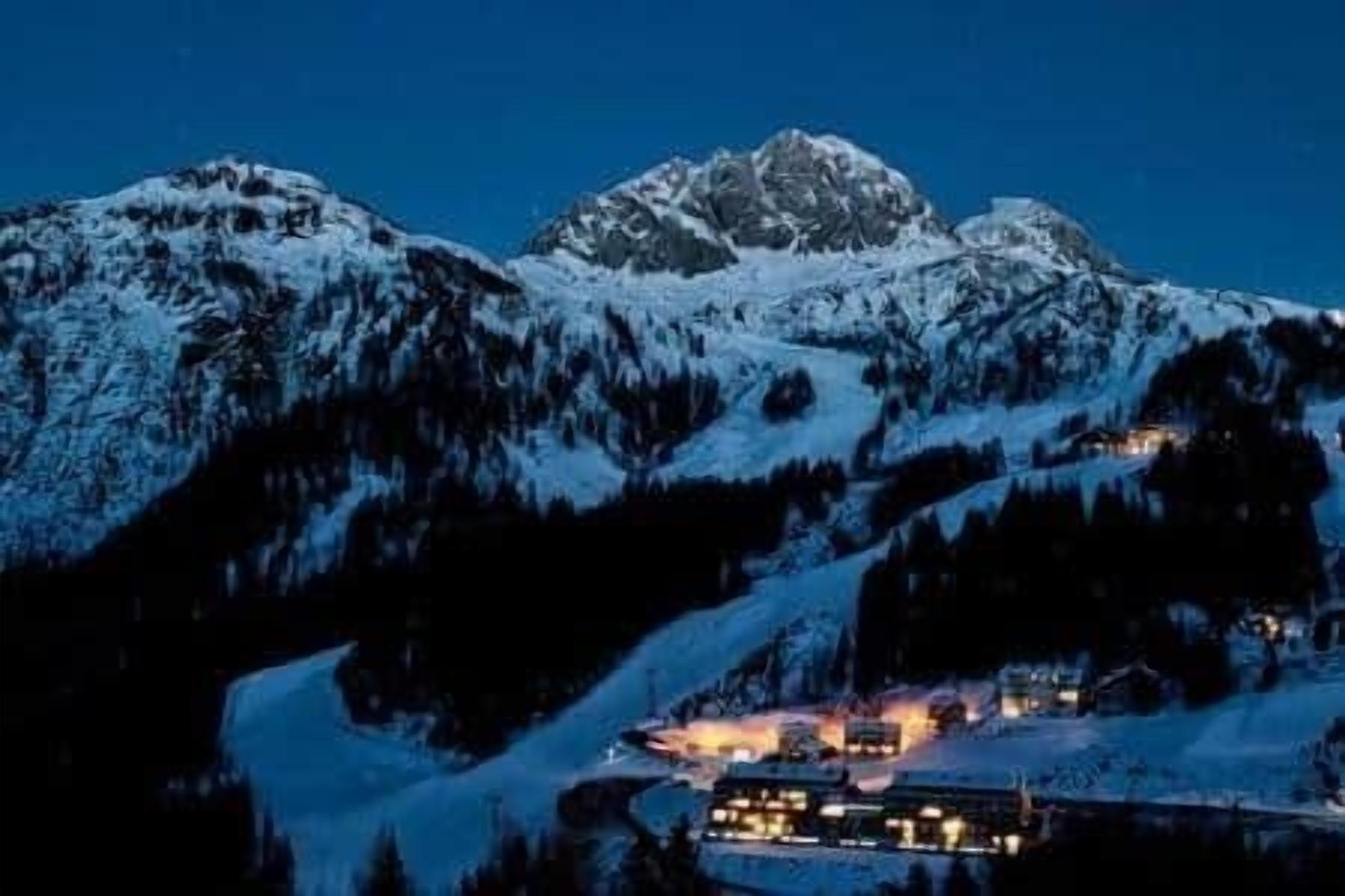 A snow-covered mountain range with a lit building in the foreground.