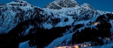A snow-covered mountain range with a lit building in the foreground.