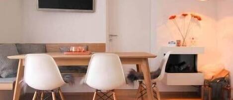 A dining area with a table and chairs, a television mounted on the wall, and a fireplace with decorative items.