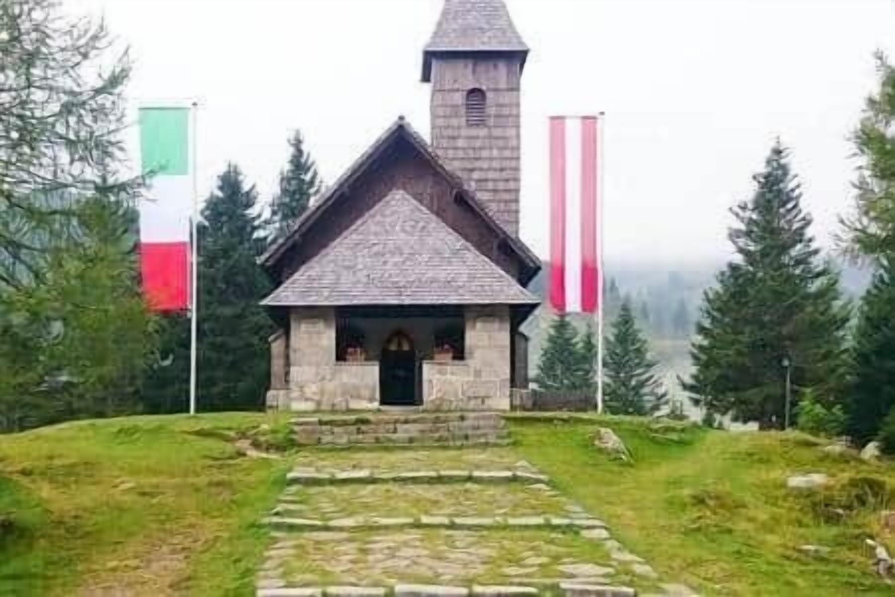 Una pequeña capilla de piedra con techo pronunciado y un campanario, rodeada por un sendero de piedra y vegetación.