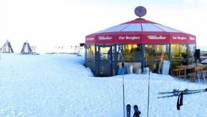 Un área al aire libre cubierta de nieve con una carpa roja con la etiqueta 'Zilberberg'.