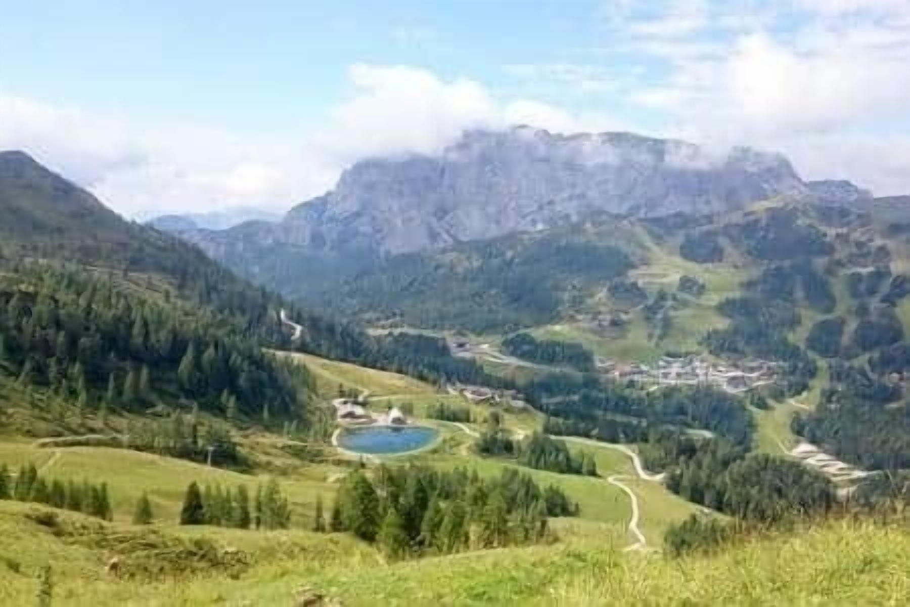 A mountainous landscape with a winding road, a small lake, and a cluster of buildings.