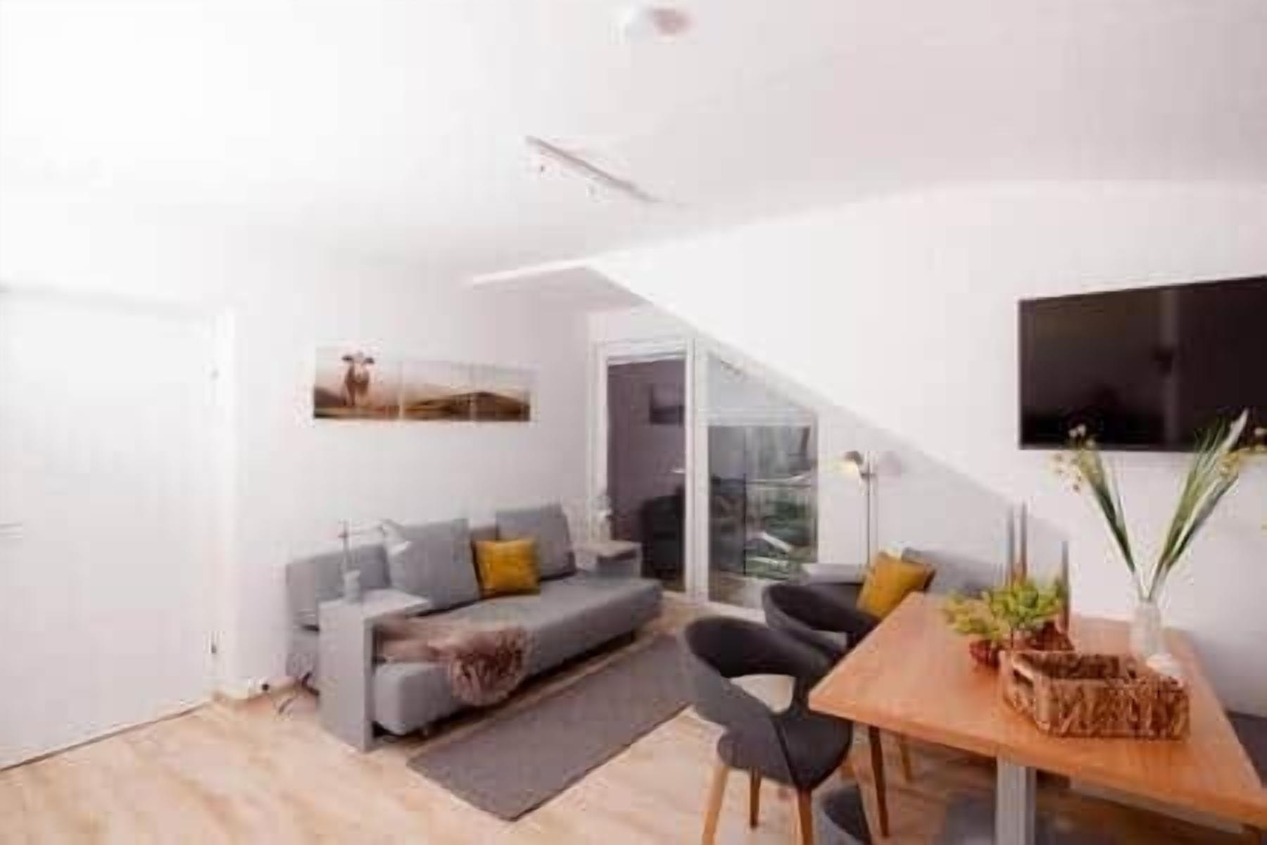 Ein modernes Wohnzimmer mit einem grauen Sofa, einem Holzesstisch und einem an der Wand montierten Fernseher.