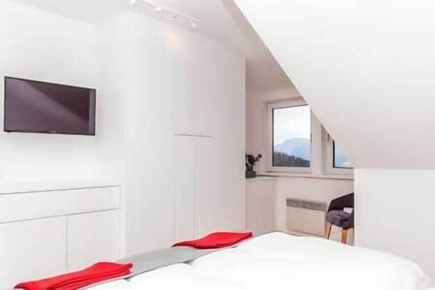 A modern bedroom with a bed, a flat-screen TV, and a window with a view.