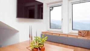 Una habitación con una televisión de pantalla plana en la pared, una ventana con vistas y un banco con una planta.