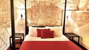 Ein Bett mit roter Decke und Kissen, eine Steinwand sowie zwei Nachttische mit Lampen.