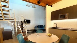 Eine moderne Küche mit integriertem Mikrowellenherd, ein Essbereich mit rundem Tisch und zwei Stühlen sowie eine Treppe, die in eine obere Ebene führt.