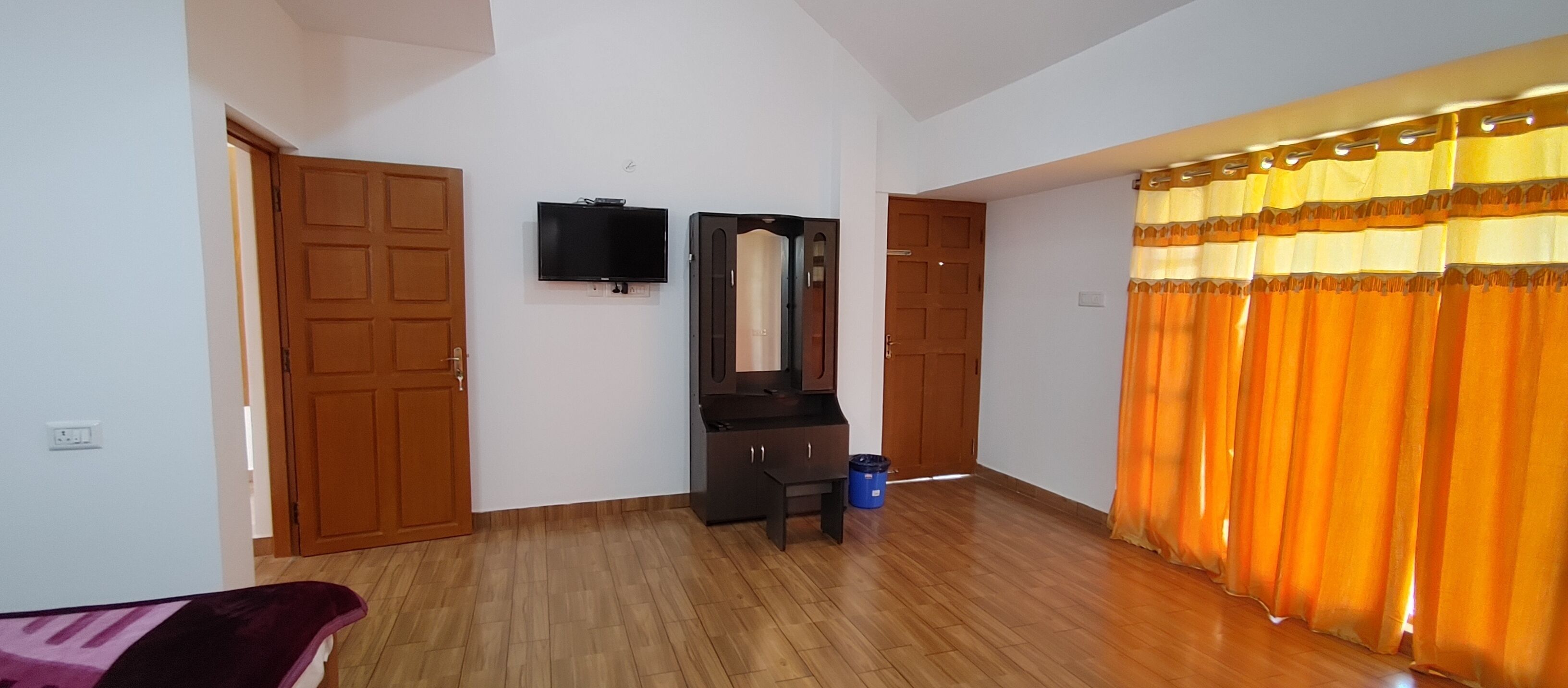 Une pièce avec un plancher en bois, un téléviseur fixé au mur, un miroir au-dessus d’une commode et un rideau à motifs rayés.