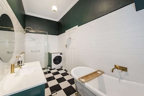 A bathroom with a checkered floor, a sink, a bathtub, a washing machine, and a mirror.