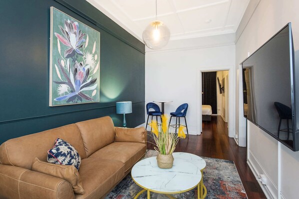 A living room with a brown sofa, a round coffee table, a painting, and a TV.