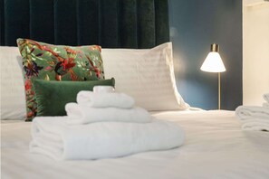A neatly made bed with folded white towels, a green floral pillow, and a bedside lamp. - Stylish 1BR APT in West Perth with Parking! (West Perth)