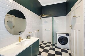 A bathroom with a white sink, gold faucet, and a round mirror.