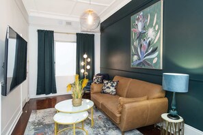 Ein Wohnzimmer mit einem braunen Sofa, einem runden Couchtisch, einer Lampe und einem Gemälde an der Wand.