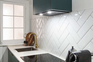 A kitchen with a white herringbone tile backsplash, a stainless steel sink, and a black coffee maker.