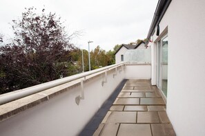 A narrow outdoor corridor with a stone floor, a white wall, and a metal railing.