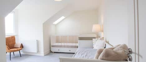 Una habitación infantil con una cuna, una cama, una silla y un radiador.