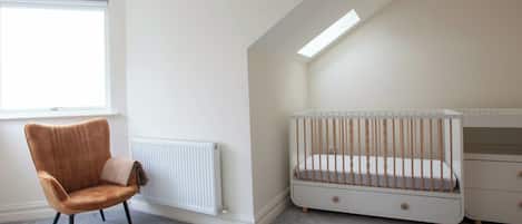 Una habitación con una silla marrón, una cuna blanca y un radiador.