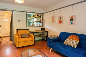 A living room with a sofa, armchair, coffee table, and a kitchen area visible through a glass door. - 1BDR Garden Retreat | Rustic Kitchen | Free WiFi (Greater Manchester)