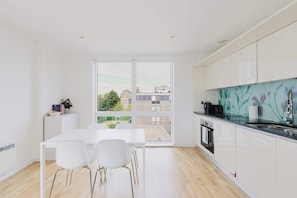 A modern kitchen with white cabinets, a dining area with a white table and chairs, and a view of buildings through large windows.