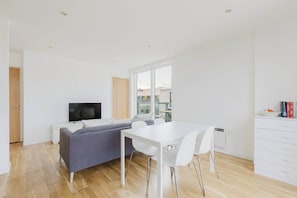 A modern, well-lit room with a sofa, a TV, a dining table, and a white cabinet.