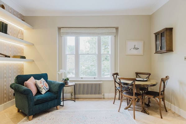 Une pièce chaleureuse avec un canapé de couleur turquoise, une table à manger avec des chaises, un radiateur et une fenêtre donnant sur un paysage verdoyant.