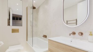 Un baño moderno con ducha envuelta en vidrio, una bañera blanca y un tocador con gabinete de madera.