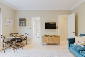 A modern living room with a dining area, a TV mounted on the wall, and a blue sofa with a patterned pillow. - Elegantly Renovated 2BD w Balcony in Notting Hill (Greater London)
