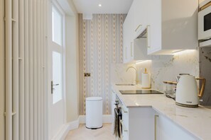 A modern kitchen with a marble countertop, a built-in oven, and a coffee maker. - Elegantly Renovated 2BD w Balcony in Notting Hill (Greater London)