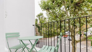 Un balcón con una mesa y dos sillas, con vista a una calle con coches aparcados y árboles.