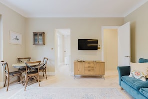 Un salon moderne comprenant un coin repas, un téléviseur fixé au mur et un canapé bleu agrémenté d’un coussin à motifs.