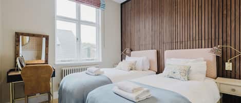 Habitación de hotel con dos camas, un escritorio, una silla, un espejo y una ventana con cortinas.