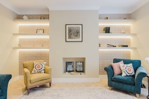 Un salon avec deux fauteuils, une cheminée et des étagères ornées d’objets décoratifs.