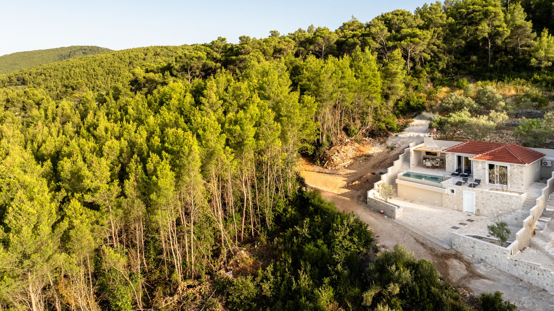 A modern villa with a pool, surrounded by dense forest and hills.