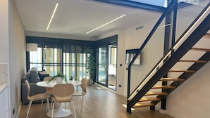 Un interior moderno con comedor, sofá, escalera y ventanas amplias.