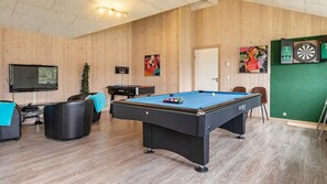 Una sala recreativa con mesa de billar, asientos, televisión y dardos.