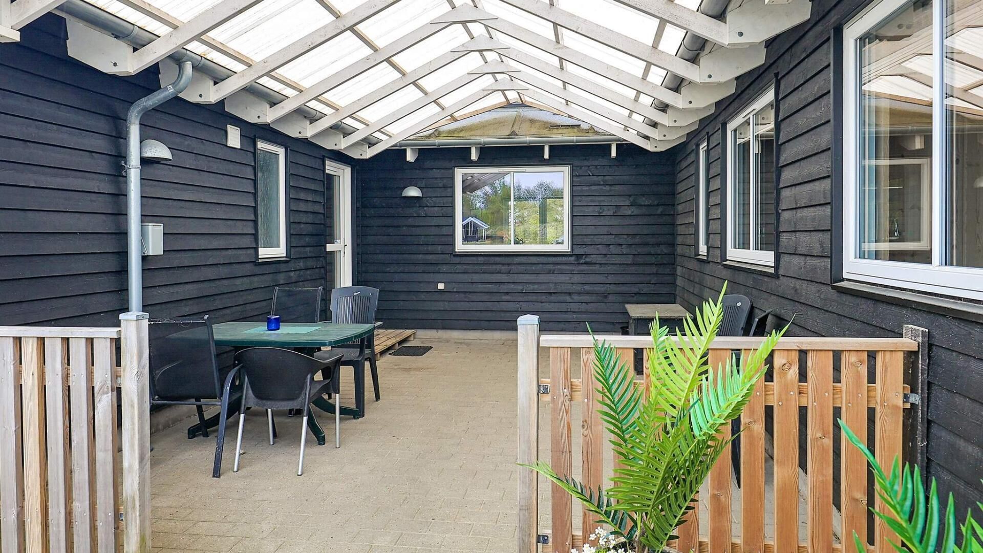 A covered outdoor patio with a table and chairs, a wooden fence, and a view of the outside.