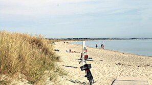A sandy beach with a bicycle parked on the sand, a lifeguard tower, and people walking along the shore. - VillaVilla 295 - Ålbæk, Nordjylland (Ålbæk)