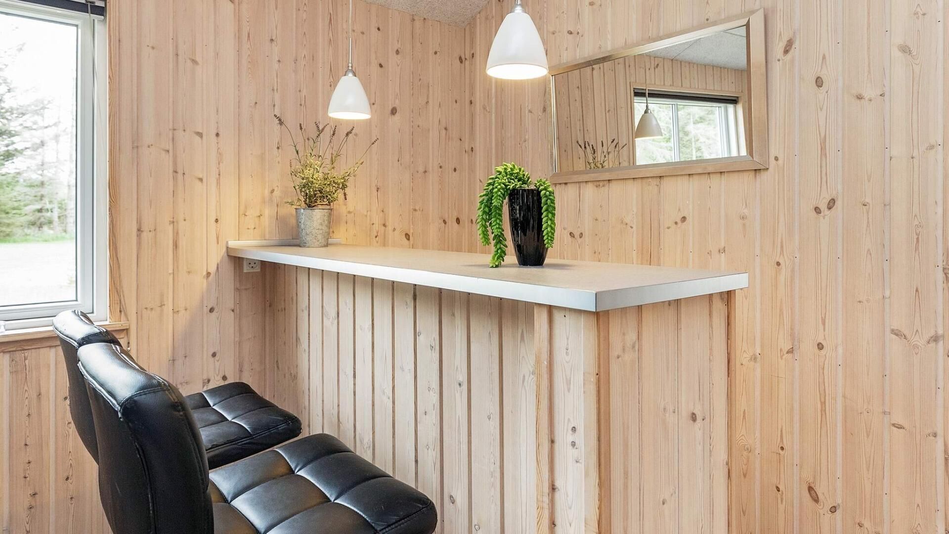 Ein Empfangsbereich mit einer Holzwand, einem weißen Empfangstresen, zwei Pendelleuchten, einem schwarzen Ledersessel und einem Spiegel über dem Tresen.