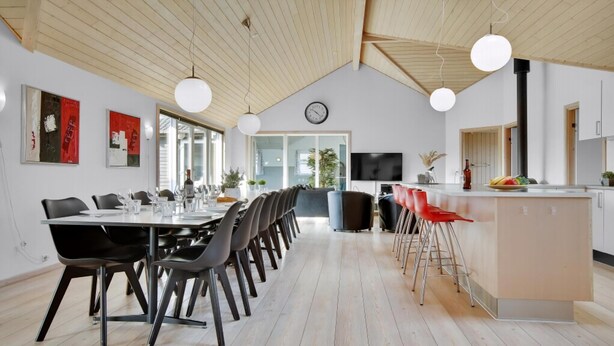A modern kitchen with a bar area, wooden flooring, and a dining area with a long table and chairs. - VillaVilla 194 - Nr. Lyngby ved Løkken, nordjyllan (Løkken)