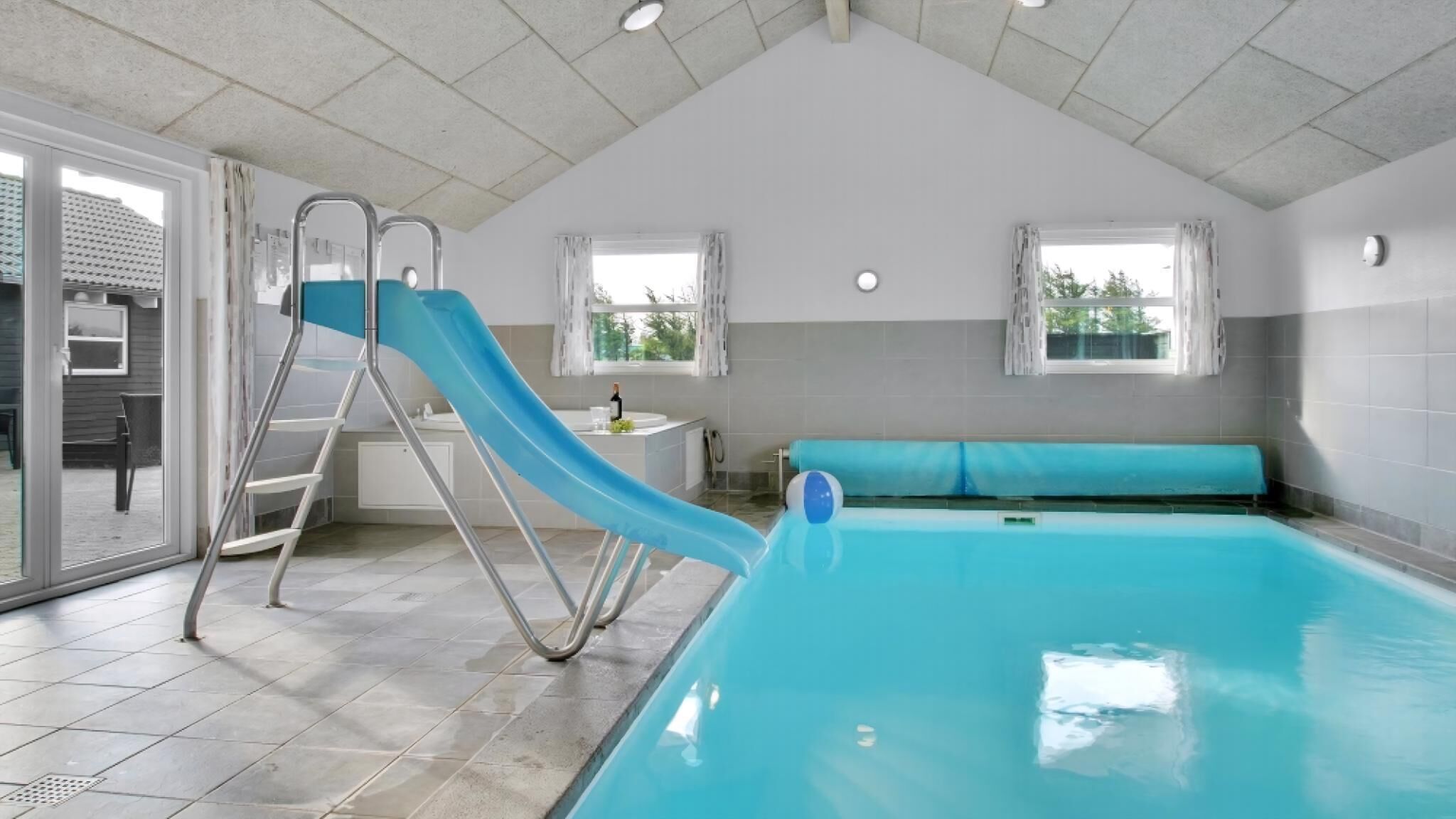 Une piscine avec un toboggan, un banc et une petite table sur laquelle se trouve une bouteille.
