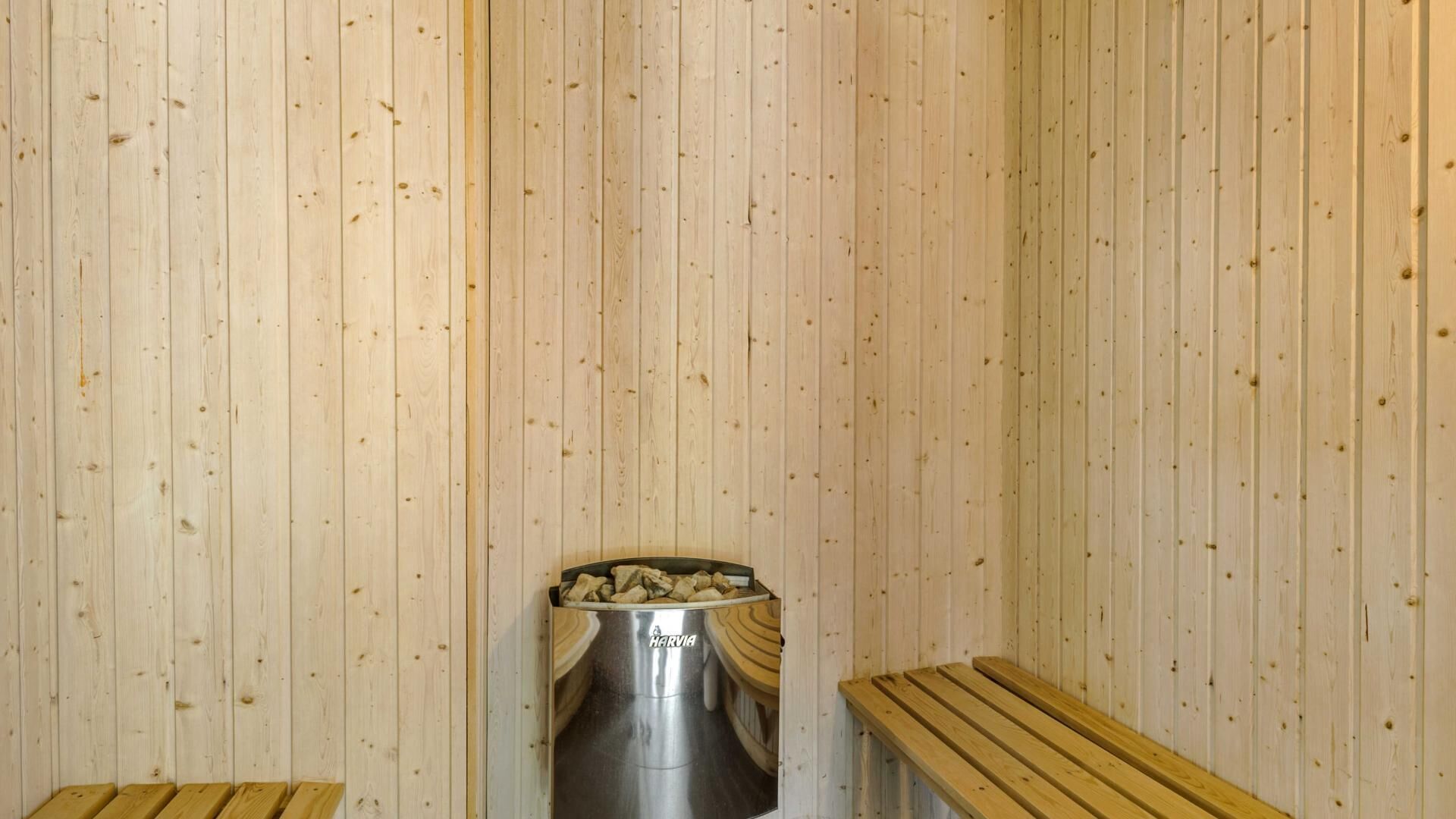 Een sauna met houten wanden, een metalen bak met stenen en houten banken.
