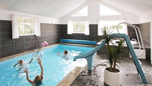 Une piscine intérieure avec un toboggan bleu, une plante en pot et un mur carrelé.