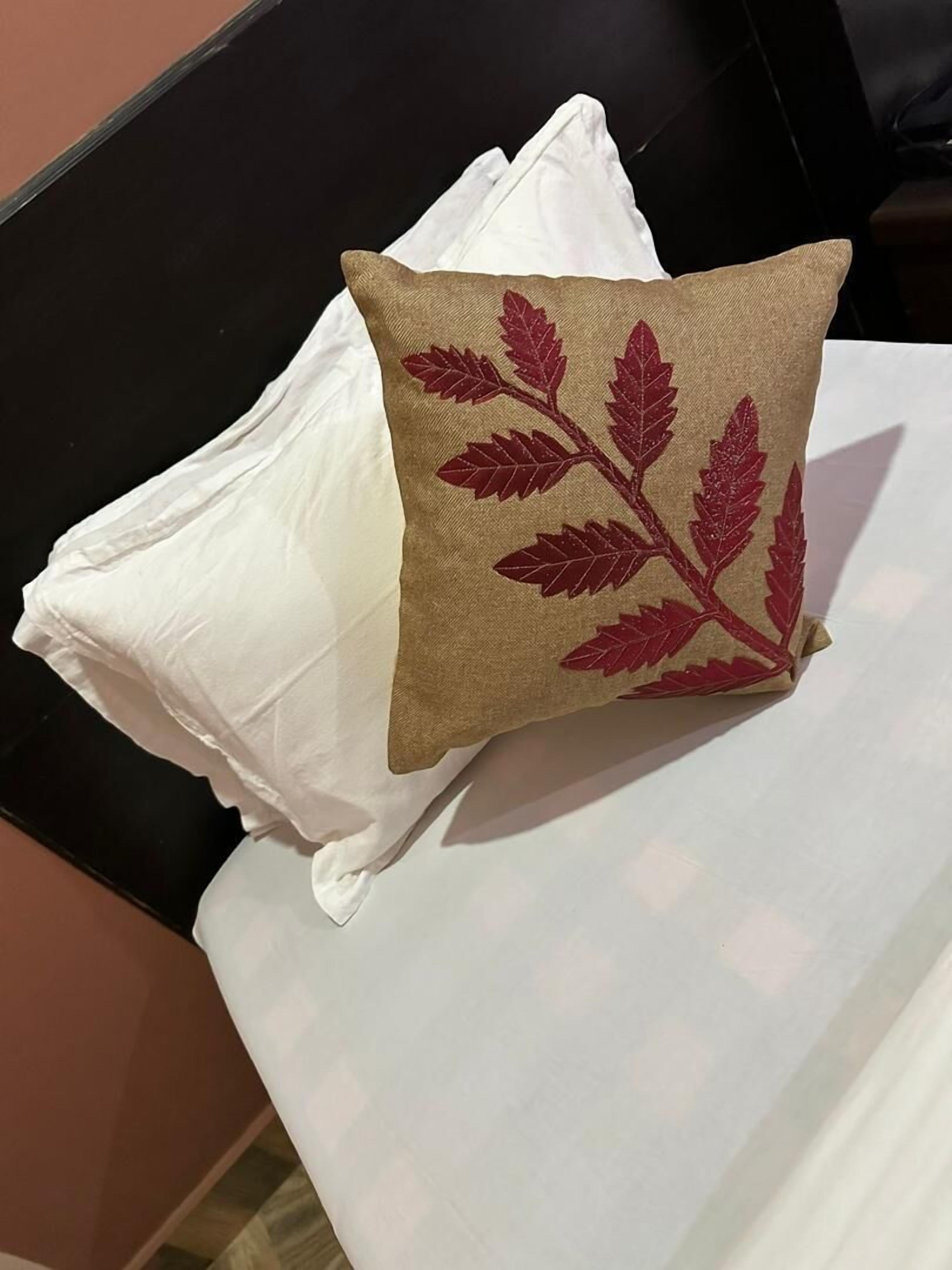 A bed with white pillows and a single decorative pillow with a leaf pattern.