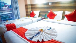 A hotel room with two beds, each with a red pillow, white linens, and a red blanket. There are decorative towels on the beds. - Paundur Community Homestay (Pokhara)