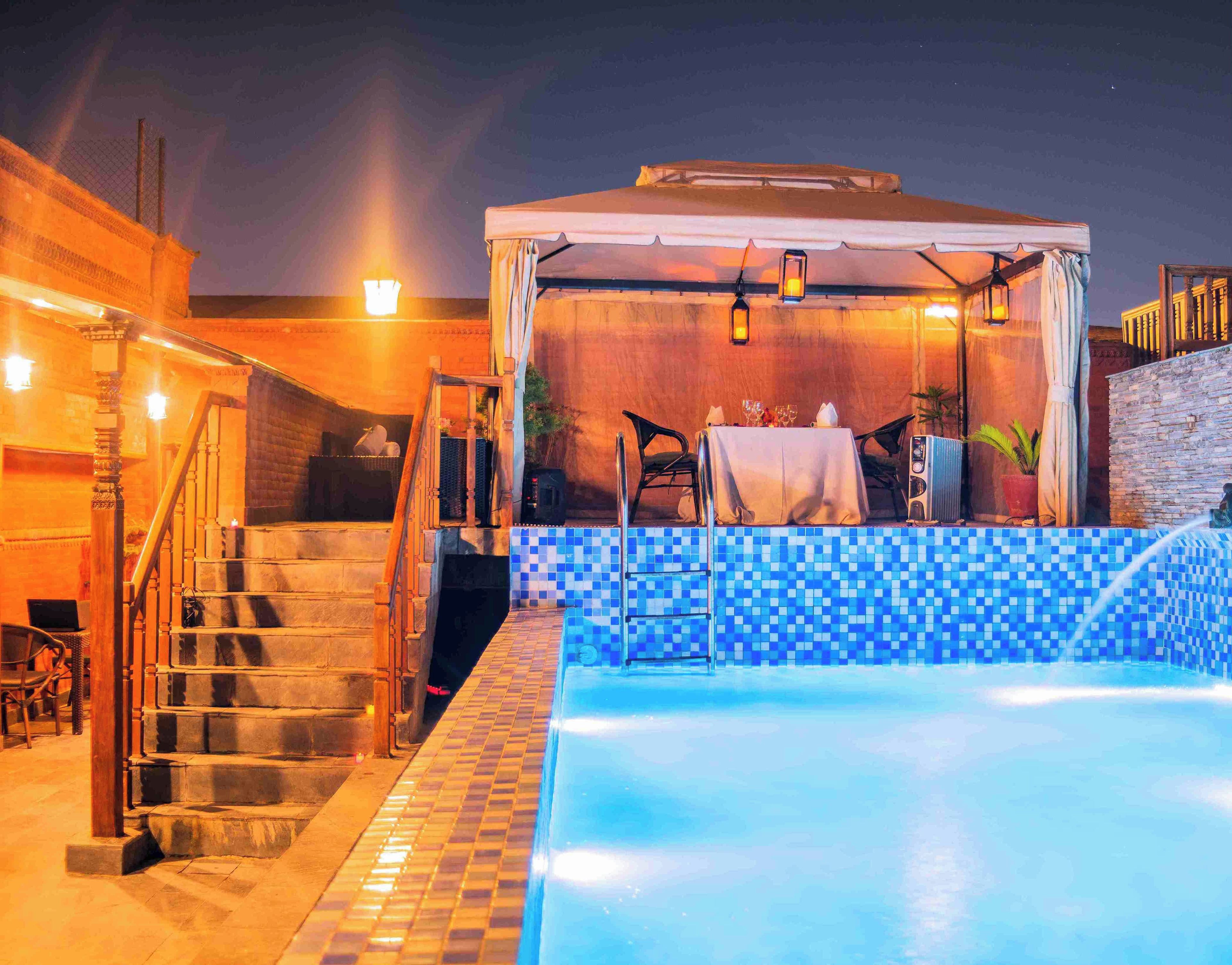 A pool area with a covered seating area, stairs, and a tiled wall.