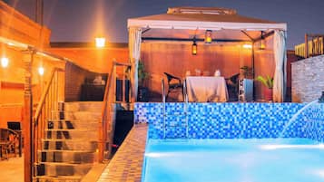 A pool area with a covered seating area, stairs, and a tiled wall.
