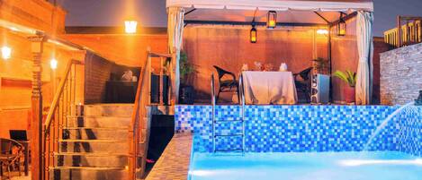 Zona de piscina con área de estar techada, escaleras y pared de azulejos.