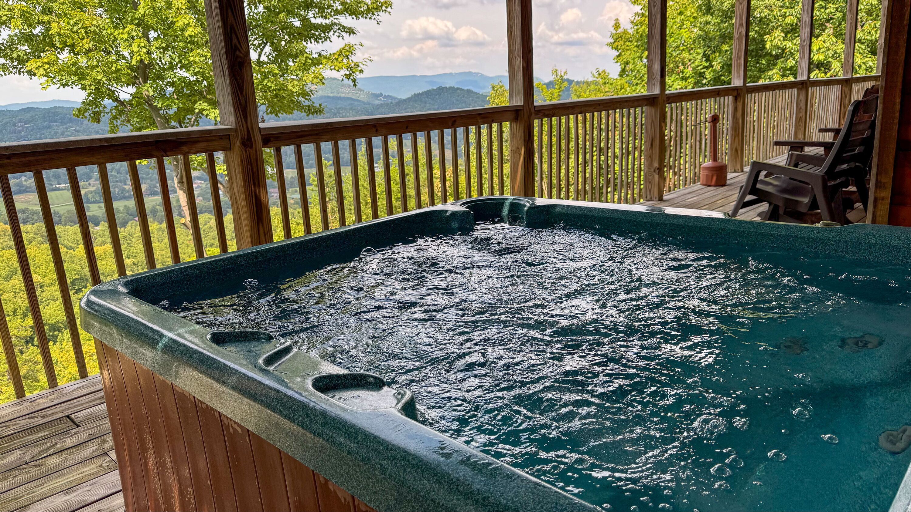 Ein Whirlpool auf einer Holzterrasse mit Blick auf Berge und Bäume.