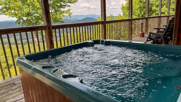A hot tub on a wooden deck with a view of mountains and trees.